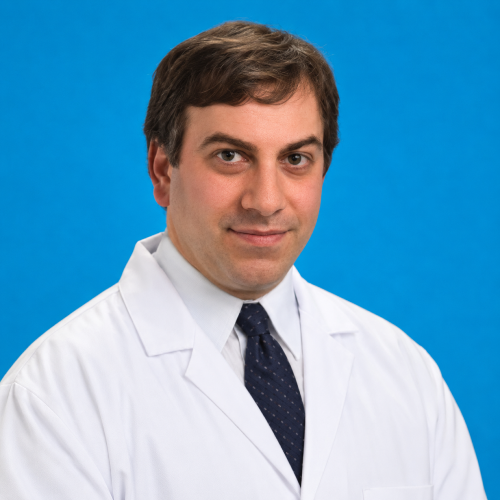A man in a white lab coat and dark tie stands against a solid blue background, looking at the camera with a neutral expression.